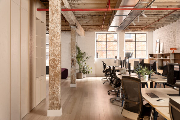 Custom shelving, timber flooring, and joinerty against painted brick walls in the Milanote Melbourne office fitout, adding texture, display space and character to the open workspace.