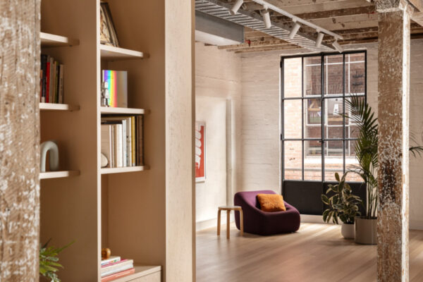 Custom shelving, timber flooring, and joinerty against painted brick walls in the Milanote Melbourne office fitout, adding texture, display space and character to the open workspace.