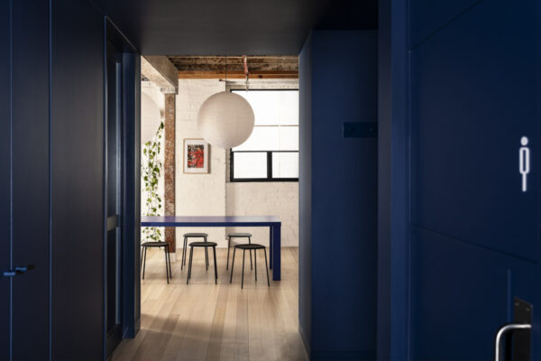 Blue-toned hallway and breakout area in the Milanote Melbourne office fitout, featuring built-in joinery, timber flooring and a minimalist shared workspace.