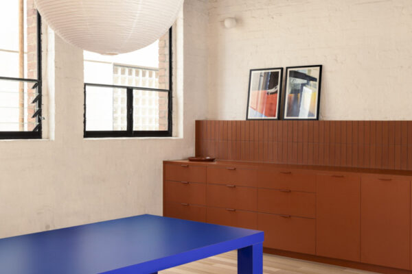 Breakout area in the Milanote Melbourne office fitout with a bold blue table, built-in cabinetry, timber floors and exposed industrial ceiling details.