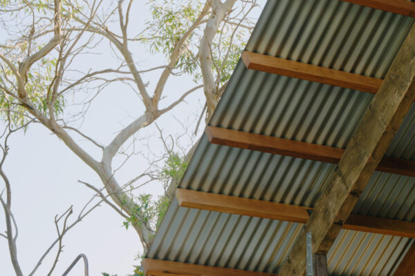 Outdoor shower area in the Glaneuse project in Point Lonsdale, Victoria, featuring a copper shower fixture, painted block wall, corrugated roof sheeting, exposed timber framing and a relaxed coastal material palette.
