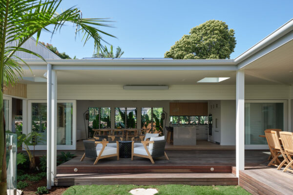 Rear outdoor living area in the Dylan Lane family home renovation in Byron Bay, featuring a covered timber deck, open-plan indoor-outdoor connection, white weatherboard cladding and landscaped garden surrounds.