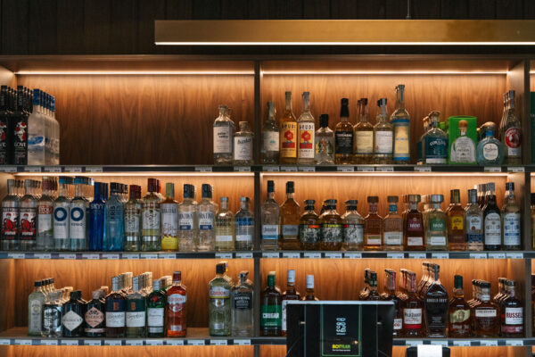 Backlit liquor display and tiled service counter in the Top Pub BottleShop fitout in Mullumbimby, featuring illuminated timber shelving, dark wall panelling and a moody retail interior.