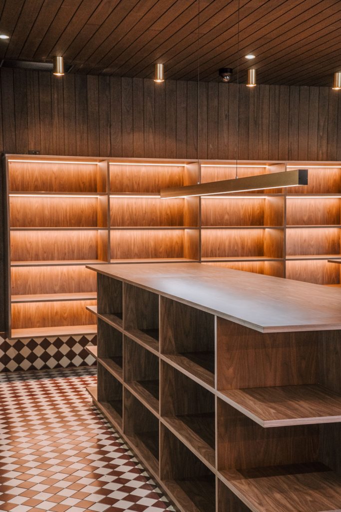 Custom timber retail display units in the Top Pub BottleShop fitout in Mullumbimby, featuring illuminated shelving, chequered floor tiles and a moody commercial interior.