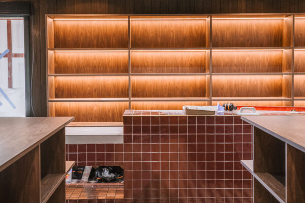 Retail fitout in the Top Pub BottleShop in Mullumbimby, featuring illuminated timber shelving, chequered floor tiles, tiled bar detailing and a dark moody interior.