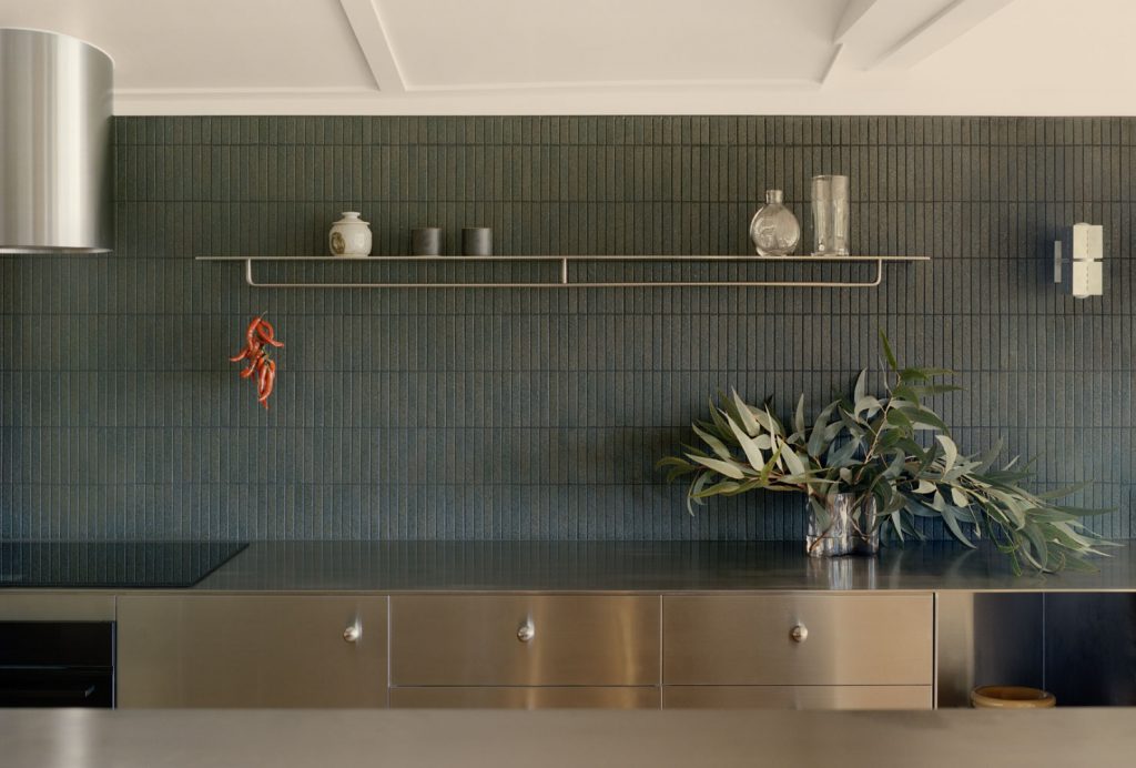 Kitchen wall detail in the Stainless Kitchen Renovation in Newrybar, featuring stainless steel cabinetry, dark tiled splashback, open shelving and a refined contemporary material palette.