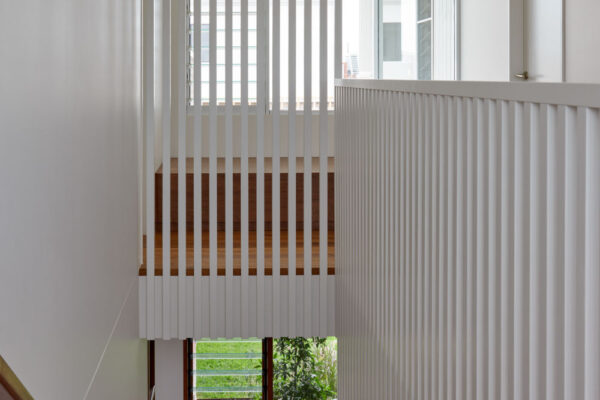 Stair void in the Sunhaven Avenue home build in Skennars Head, featuring white vertical screening, timber stair detailing, full-height glazing and a planted courtyard outlook.