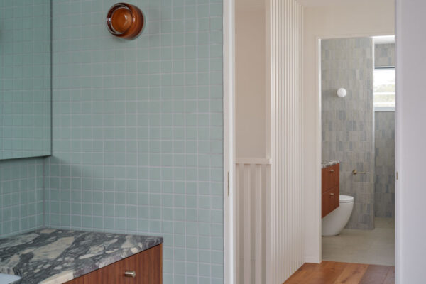 Bathroom and hallway detail in the Sunhaven Avenue home build in Skennars Head, featuring soft blue wall tiles, timber joinery, a stone vanity and white vertical screening.