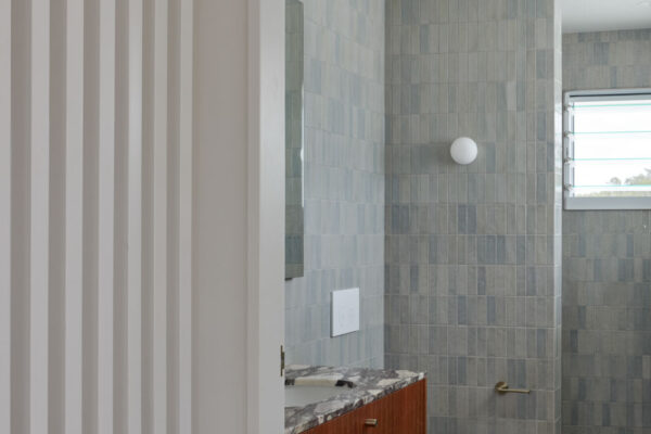 Bathroom interior in the Sunhaven Avenue home build in Skennars Head, featuring blue-grey wall tiles, timber joinery, a stone vanity and a clean contemporary finish.