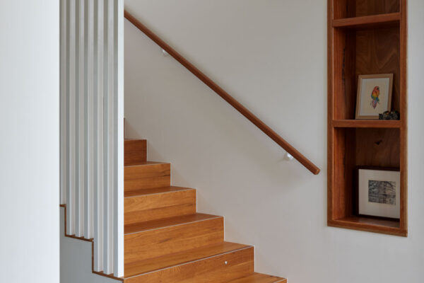 Timber staircase in the Sunhaven Avenue home build in Skennars Head, featuring white vertical screening, built-in wall shelving and a clean contemporary interior finish.