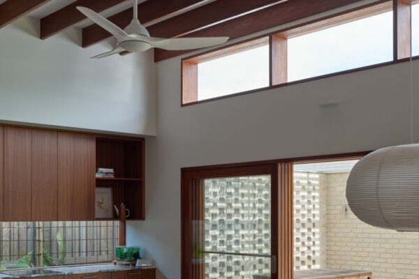 Open-plan kitchen and dining area in the Sunhaven Avenue home build in Skennars Head, featuring exposed timber beams, a stone island bench, high-level glazing and a strong connection to the outdoor living area