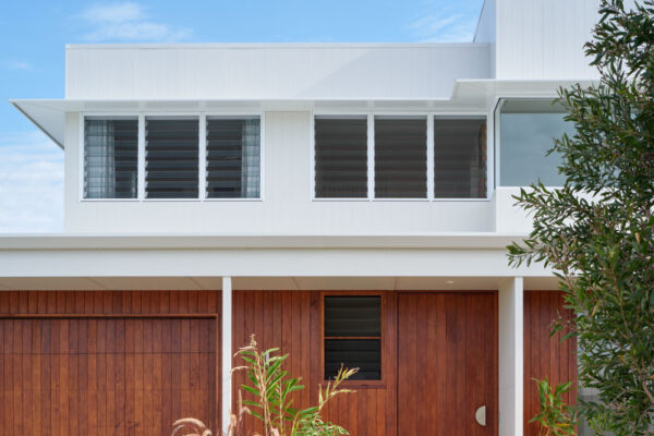 Front exterior of the Sunhaven Avenue home build in Skennars Head, featuring white upper cladding, timber garage and entry detailing, landscaped surrounds and a clean contemporary form.