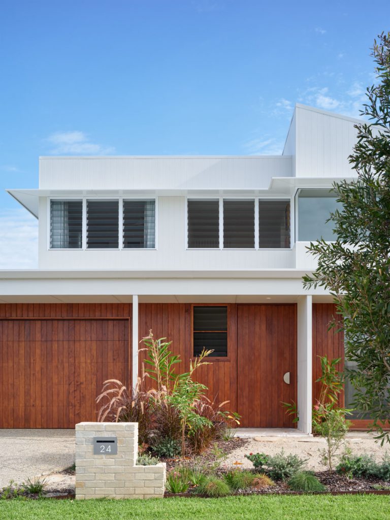 Front exterior of the Sunhaven Avenue home build in Skennars Head, featuring white upper cladding, timber garage and entry detailing, landscaped surrounds and a clean contemporary form.