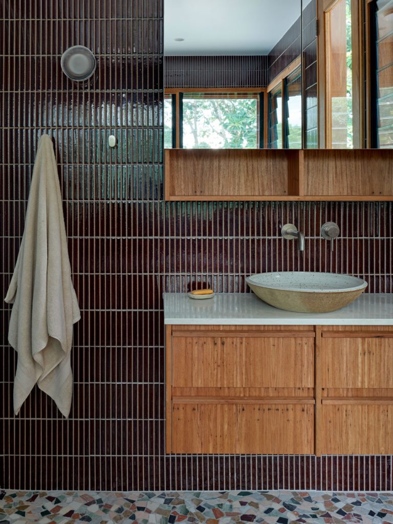 Bathroom vanity in the Left Bank Road extension in Mullumbimby, featuring dark wall tiles, timber joinery, a stone basin and a richly textured material palette.