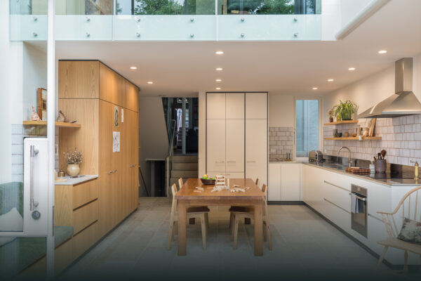 Open-plan kitchen and dining area in the Park House build in Parkville, Melbourne, featuring timber joinery, white cabinetry, double-height glazing and layered connected living spaces.