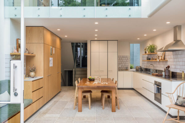 Open-plan kitchen and dining area in the Park House build in Parkville, Melbourne, featuring timber joinery, white cabinetry, double-height glazing and layered connected living spaces.