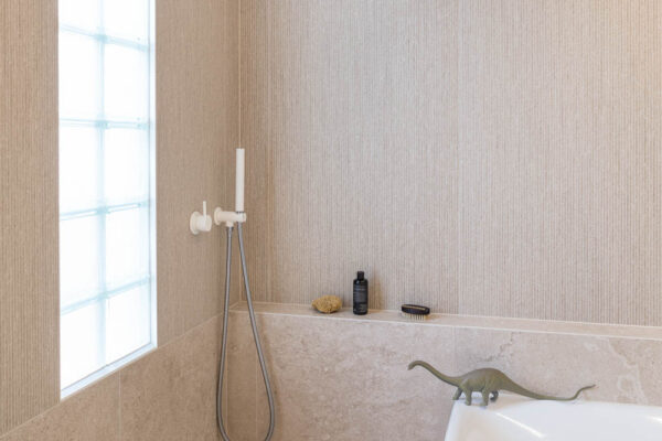 Bathroom in the Park House build in Parkville, Melbourne, featuring textured wall tiles, a freestanding bath, a glass block window and a soft natural material palette.