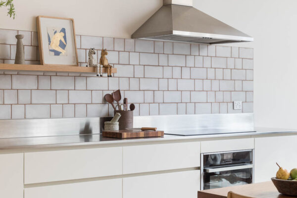 Kitchen interior in the Park House build in Parkville, Melbourne, featuring white cabinetry, a tiled splashback, stainless steel benchtop and warm timber accents.